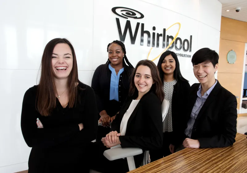 a team of students posing in front of a wall with a large Whirlpool logo