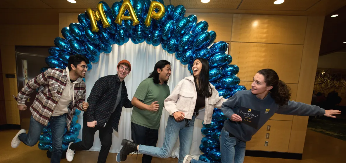 a team of students pretending to walk under a balloon arch